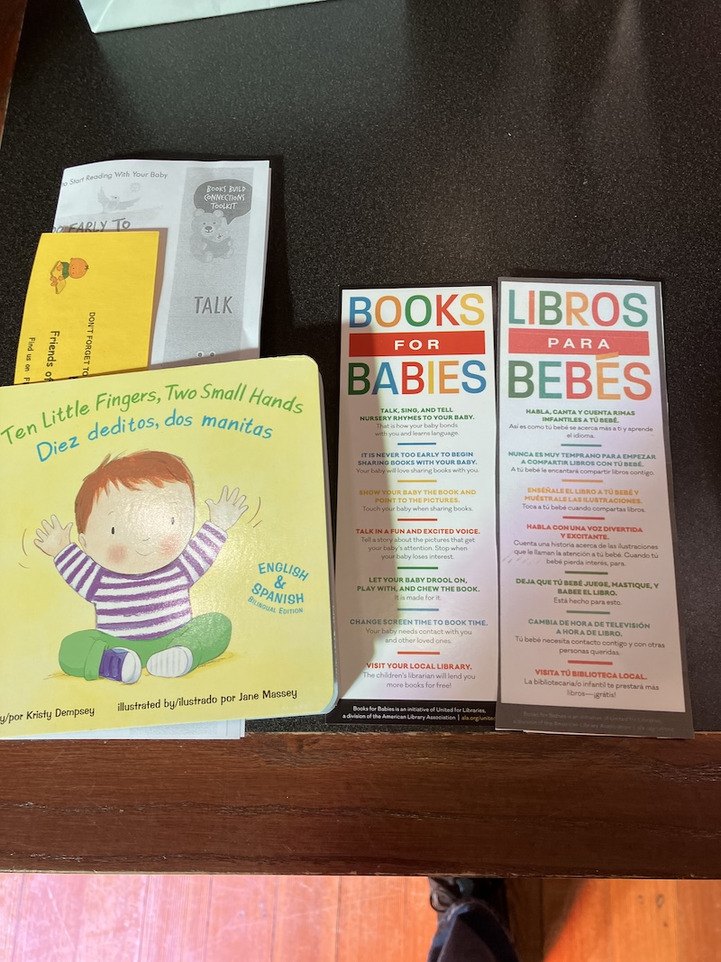 Bilingual board book 'Ten Little Fingers, Two Small Hands' alongside English and Spanish 'Books for Babies' bookmarks